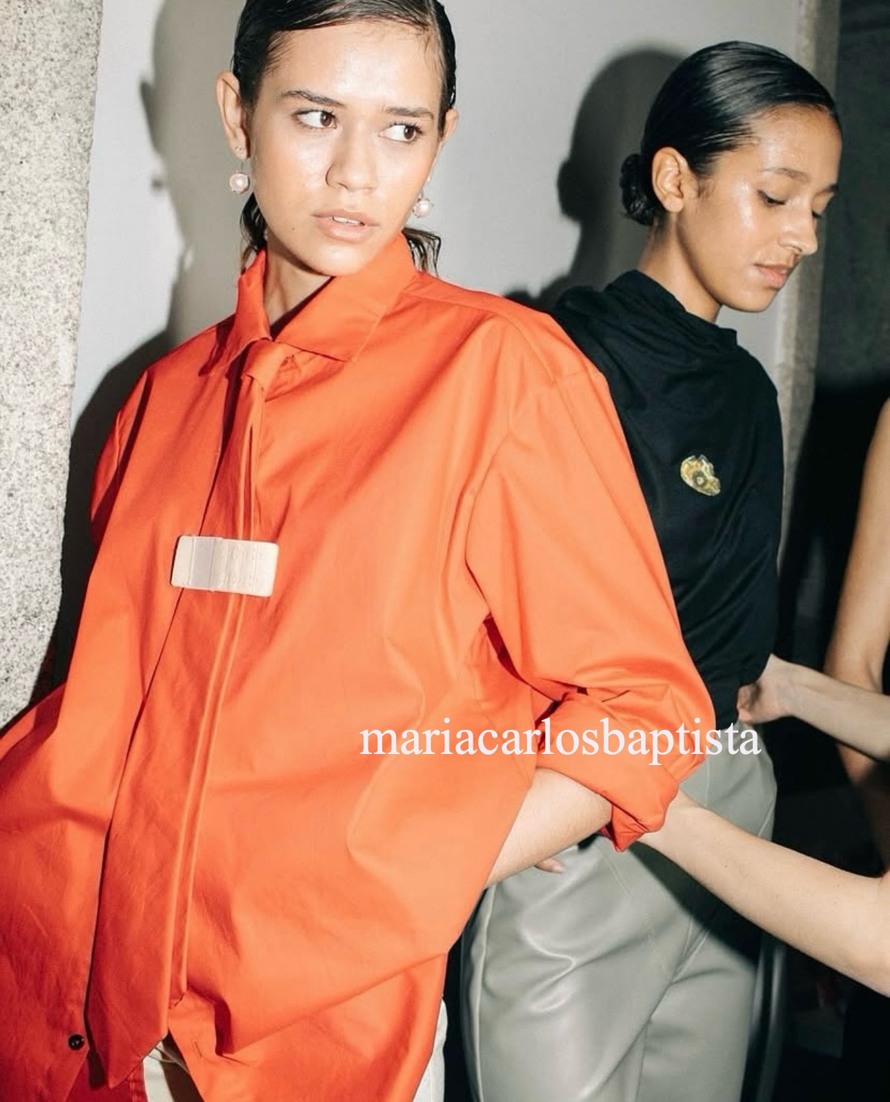 Backstage for Maria Carlos Baptista in an orange shirt and tie, with the name written across the photo