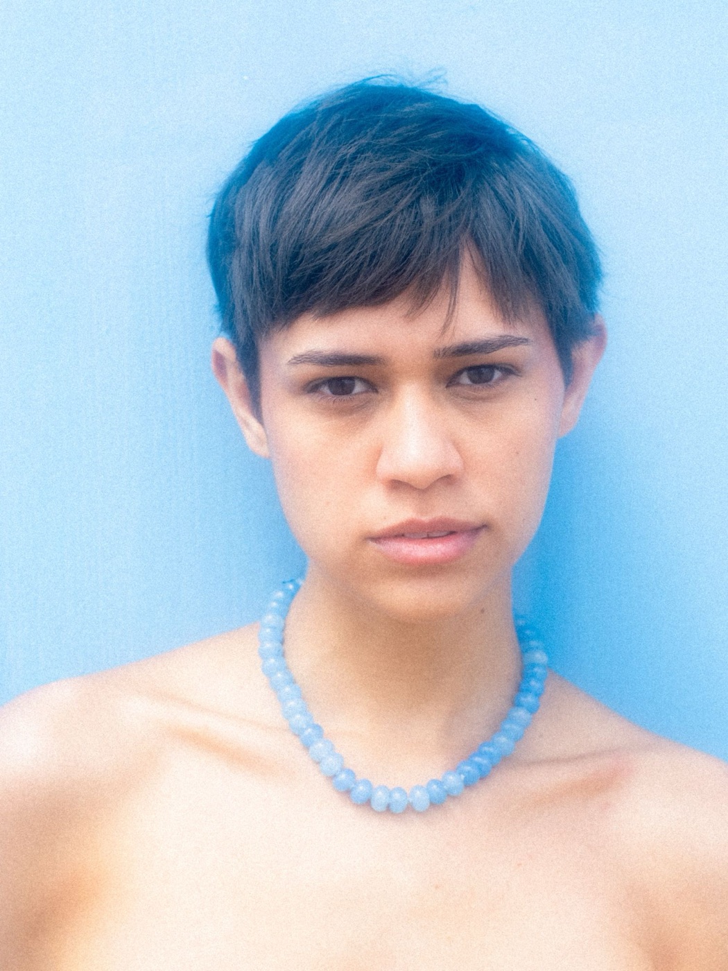Sicels: portrait against a blue wall with a blue bead necklace