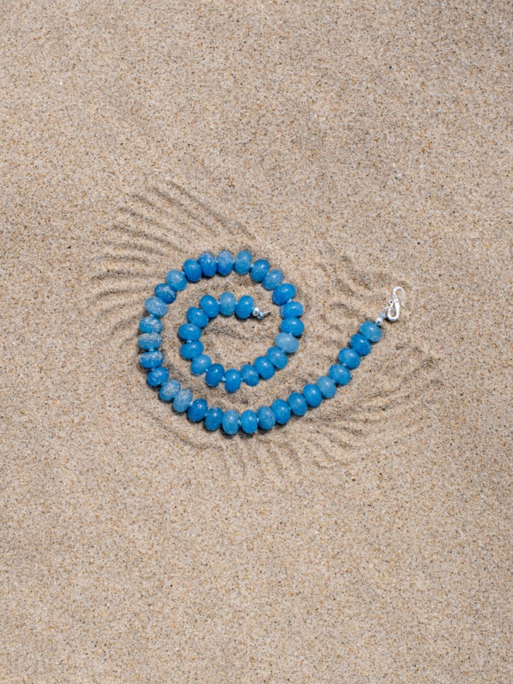Sicels: blue bead necklace coiled on the sand